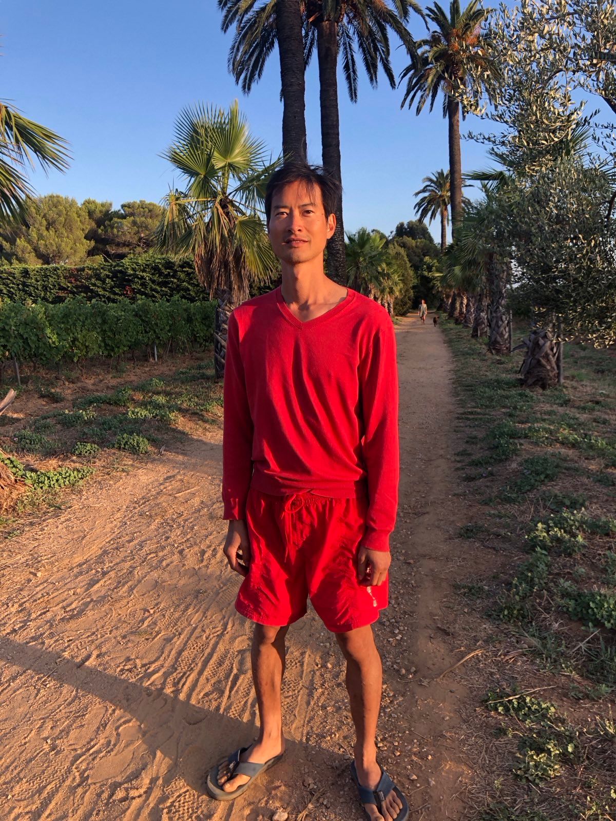 Ulysses Chuang in red, standing on a palm-lined path
